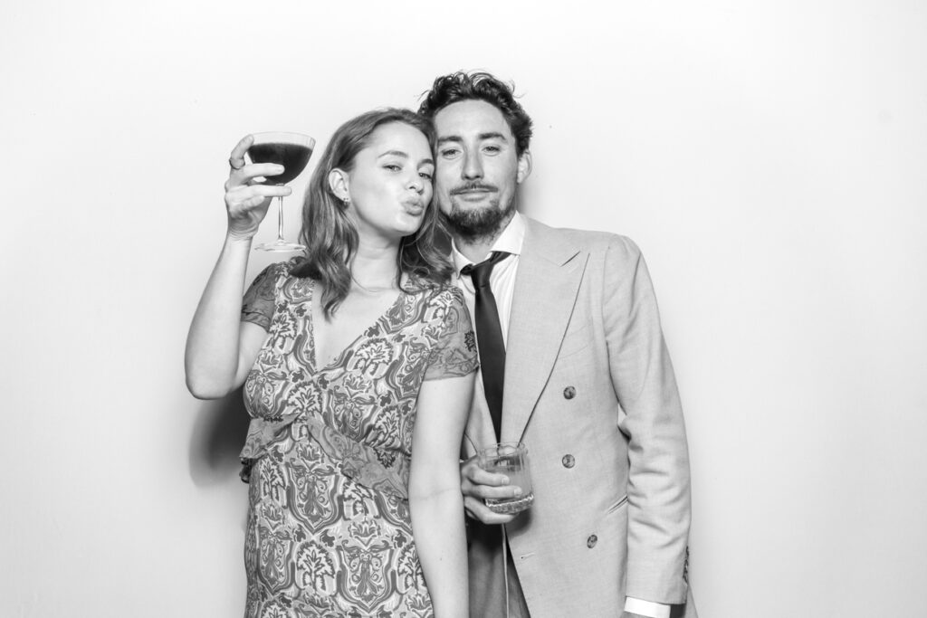 2 guests holding their glasses and posing against a white backdrop, for a Gloucester Photo Booth rental