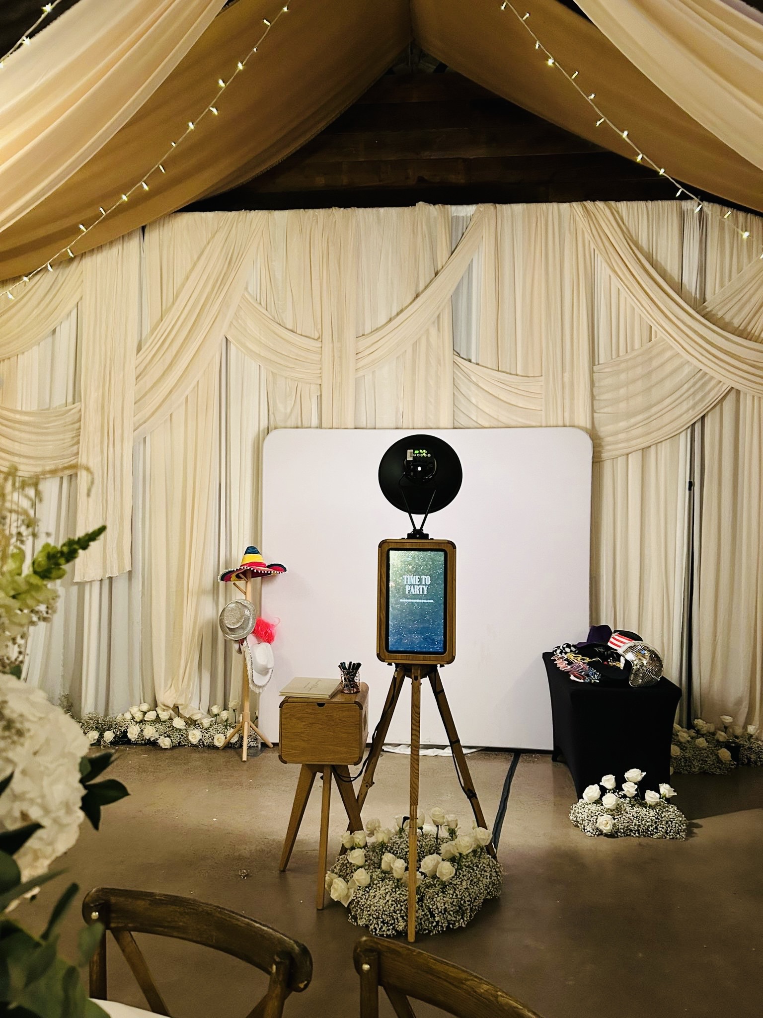 mad hat photo booth setup with the wooden photo booth and printer case, against a massive wall decorated with white fabrics, during a wedding at norton grounds