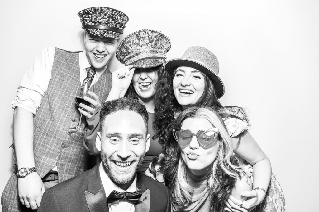 A group of guests enjoying themselves in a photo booth, wearing fun masks and hats at a wedding party entertainment, posing for mad hat photo booth rental