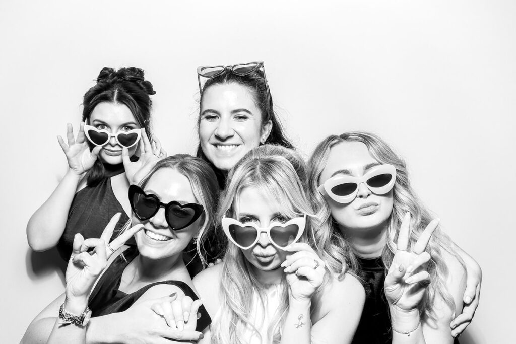 A group of friends wearing heart-shaped sunglasses and posing together for a fun shot with the black and white booth filter.