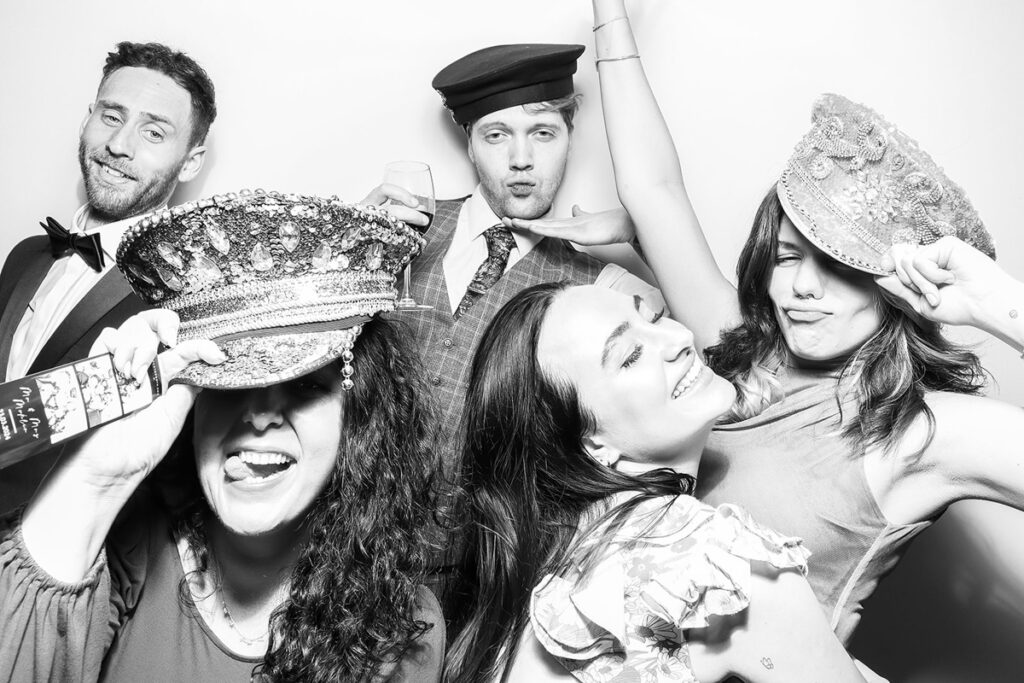  Wedding guests striking fun poses with sparkling hats and props in a photo booth at Elmore court wedding venue, with the black and white kardashian filter on