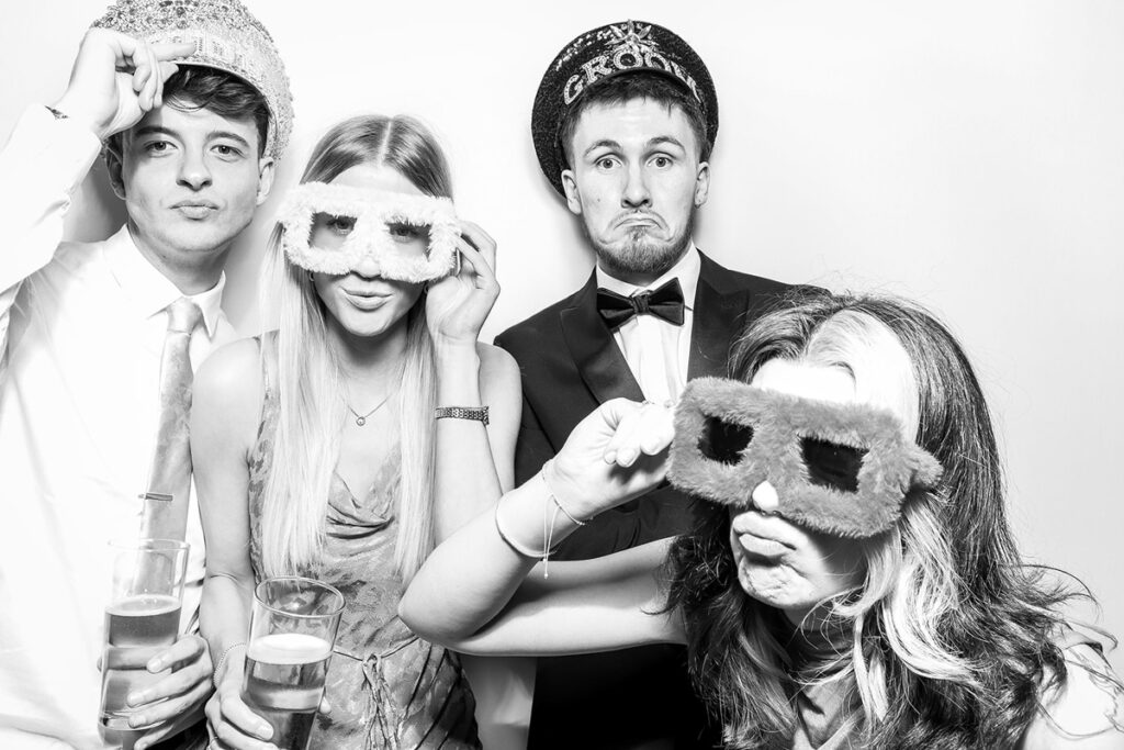 A group of wedding guests posing joyfully in a photo booth with stylish hats and playful expressions at Elmore Court