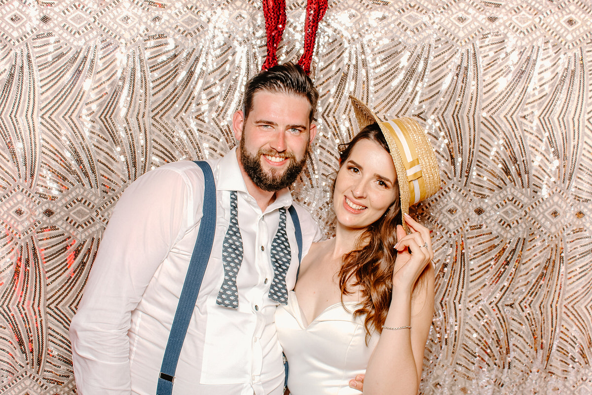 bride and groom posing for photo booth with a boho sequins backdrop 