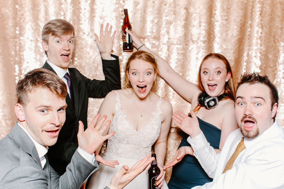 bride with guests during a cotswolds wedding, all having a fantastic time and posing against a sequins backdrop