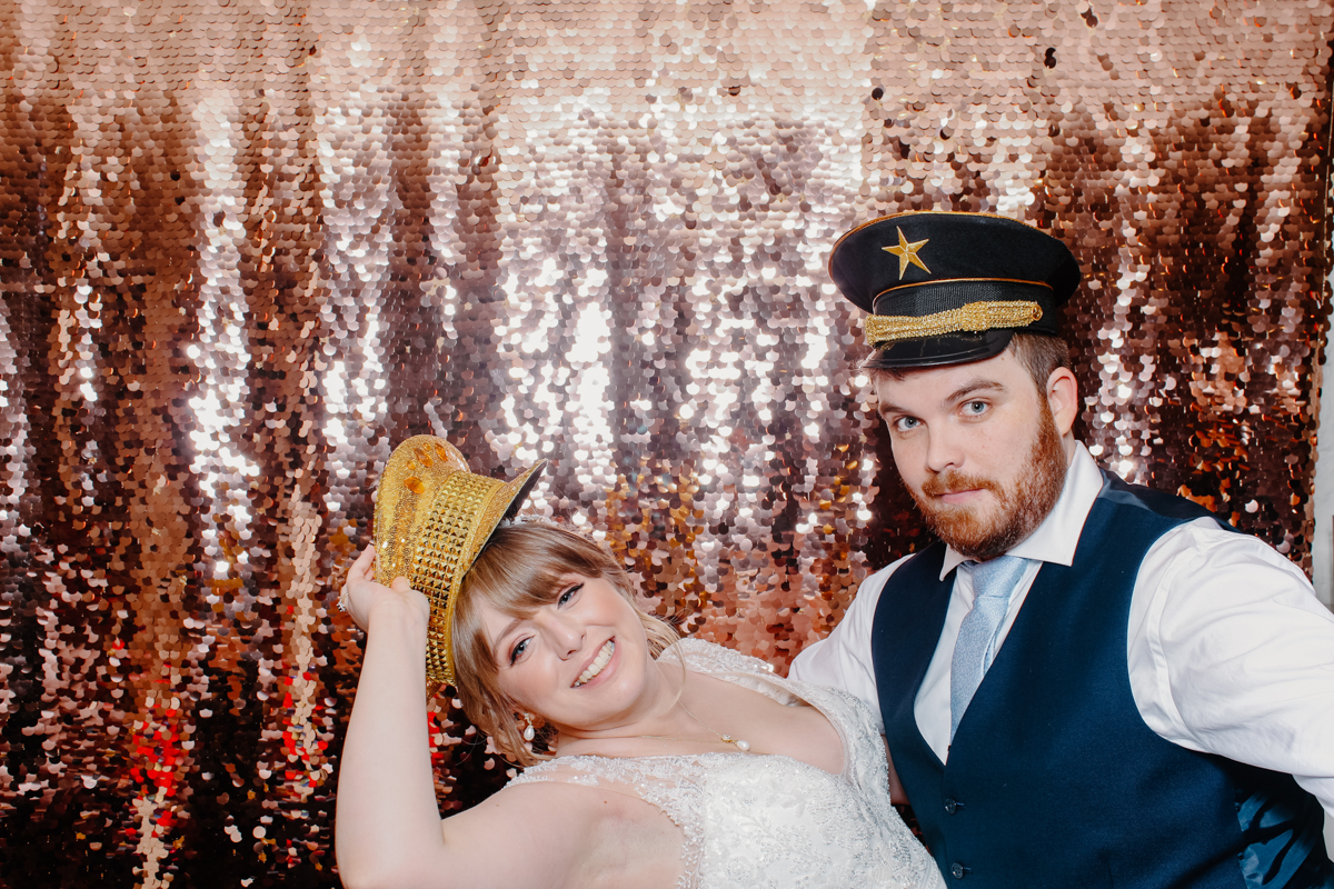 bride and groom posing for a photo booth for their Cotswolds wedding with sequins backdrop