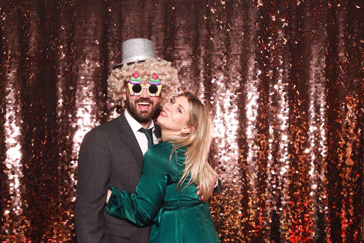 couple posing for a photo booth with a rose gold sequins backdrop 