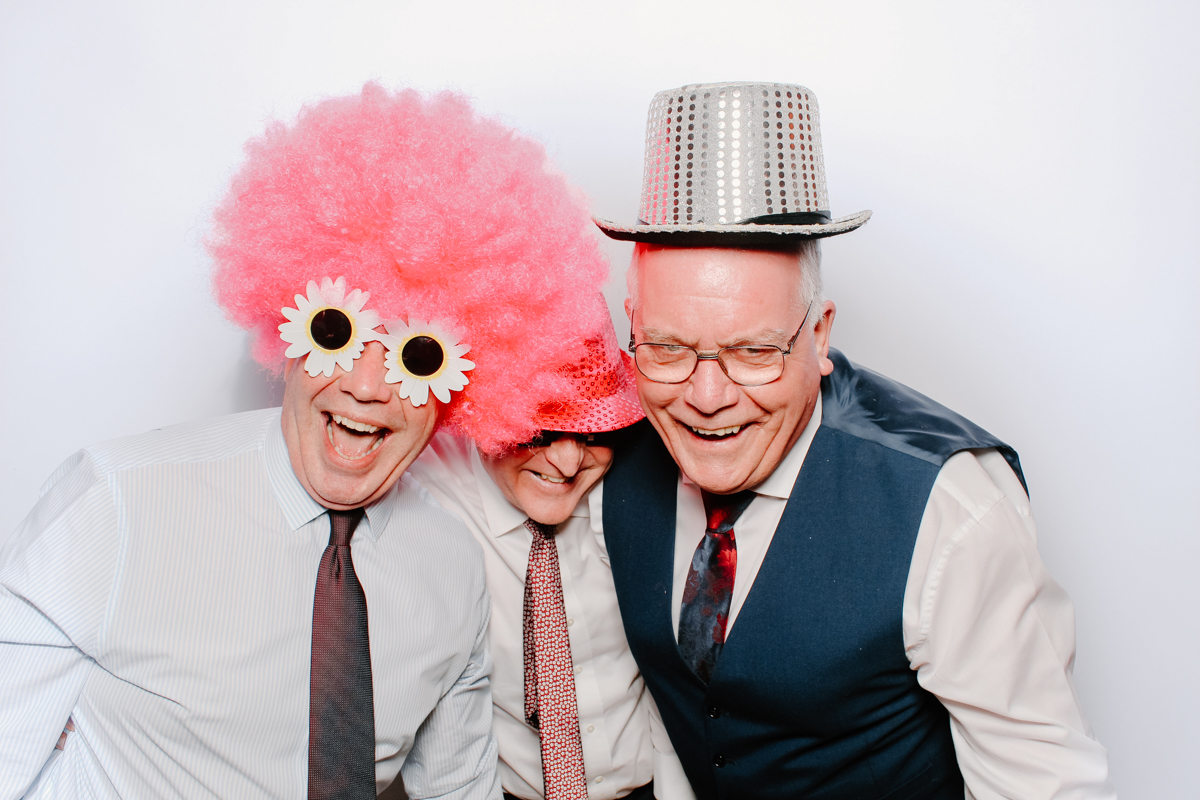 guests posing for the cotswolds photo booth wearing hats and wigs, with a white backdrop at The Swan hotel bibury