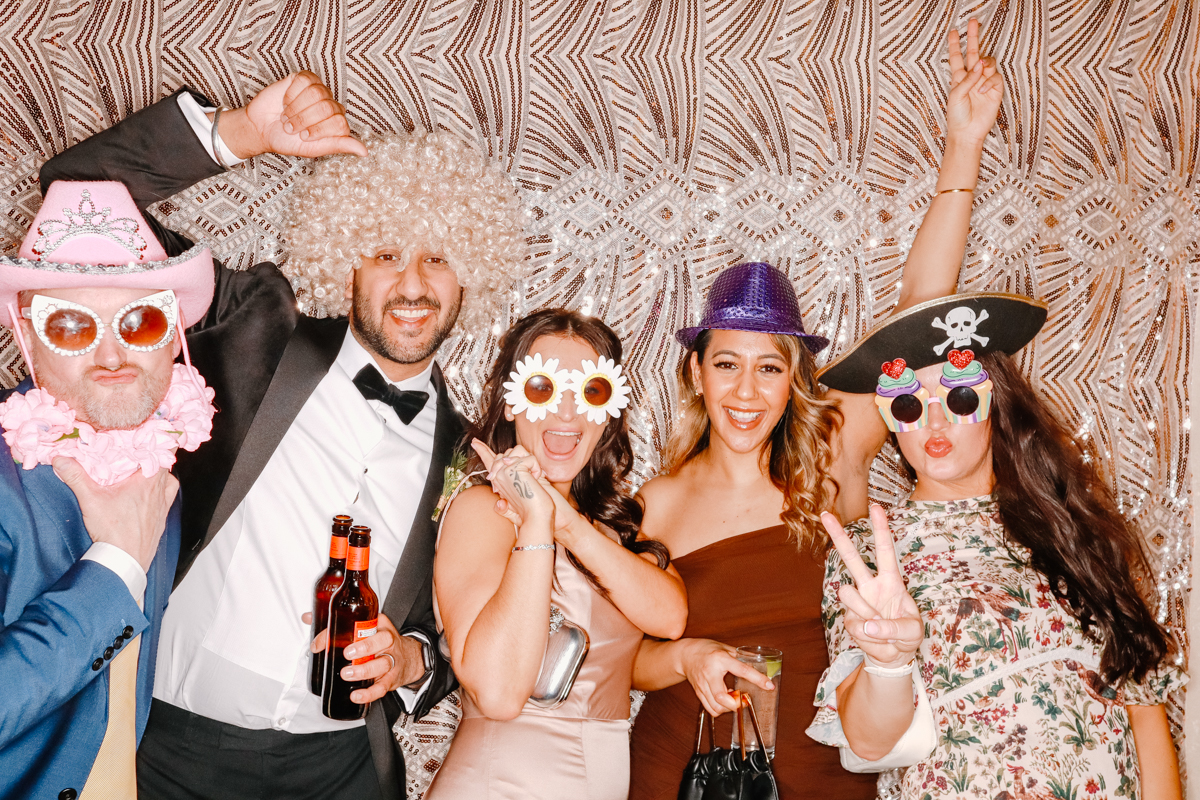 wedding guests posing for a photo booth with a sequins backdrop wall during a wedding party