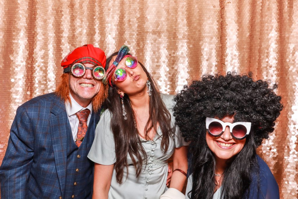 3 guests posing with props, against a blush sequins backdrop, for a Wedding Photo Booth hire in gloucester area