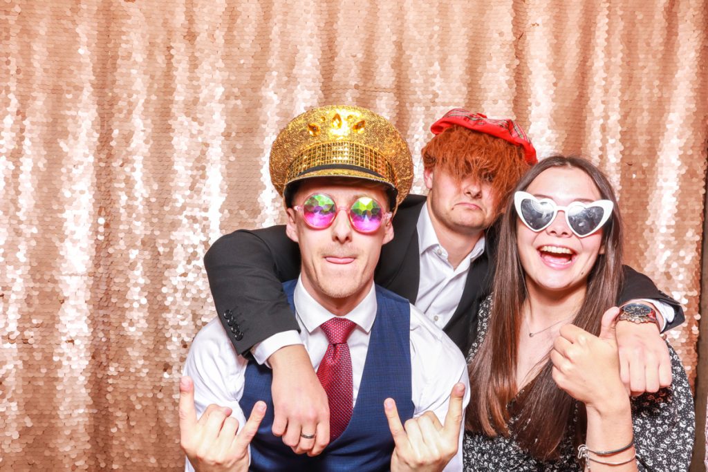 3 guests posing with props, against a blush sequins backdrop, for a Bredenbury Court Wedding Photo Booth rental