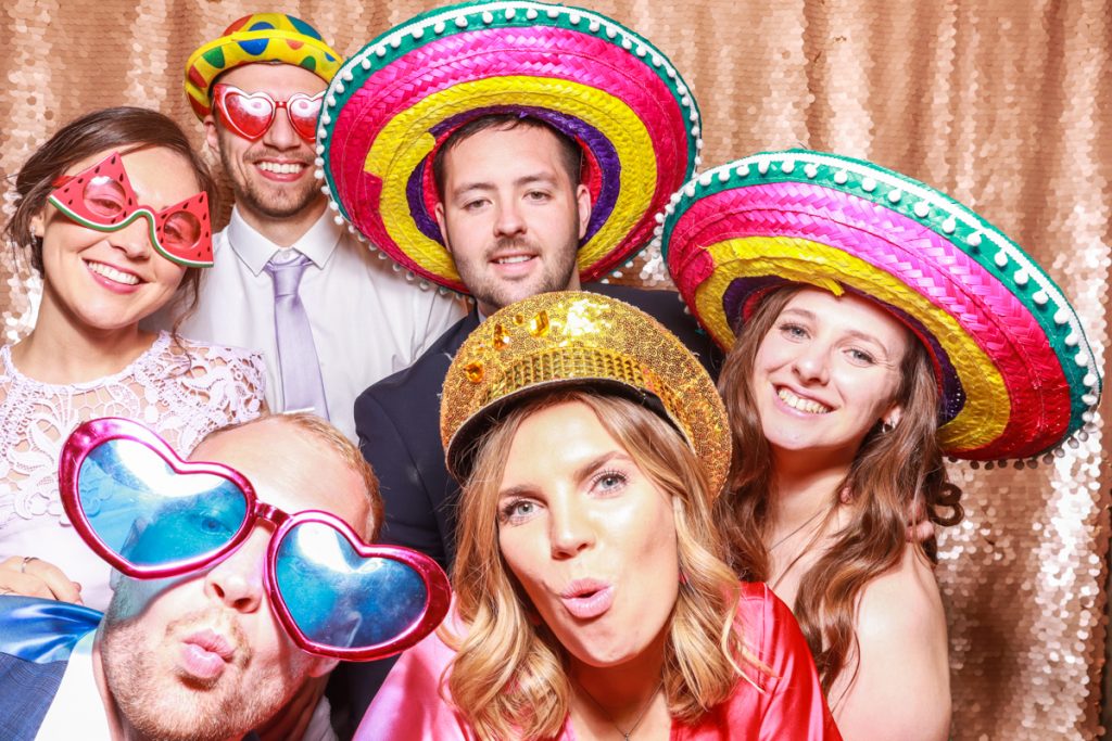 larger group of guests guests posing with props, against a blush sequins backdrop, for a Bredenbury Court Wedding Photo Booth rental