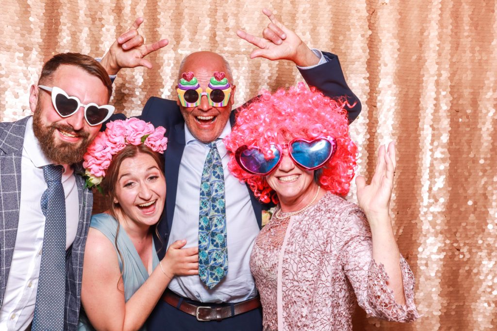 4 guests posing with props, against a blush sequins backdrop, for a Bredenbury Court Wedding Photo Booth rental