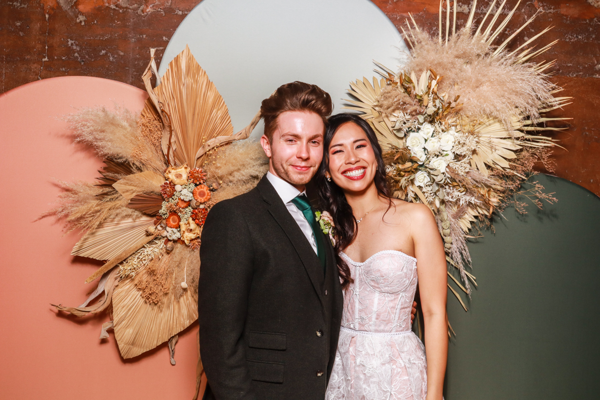 bride and groom posing against a modern arches backdrop in 3 colours, with dried flowers arrangements attached on, during an elmore court wedding venue reception party