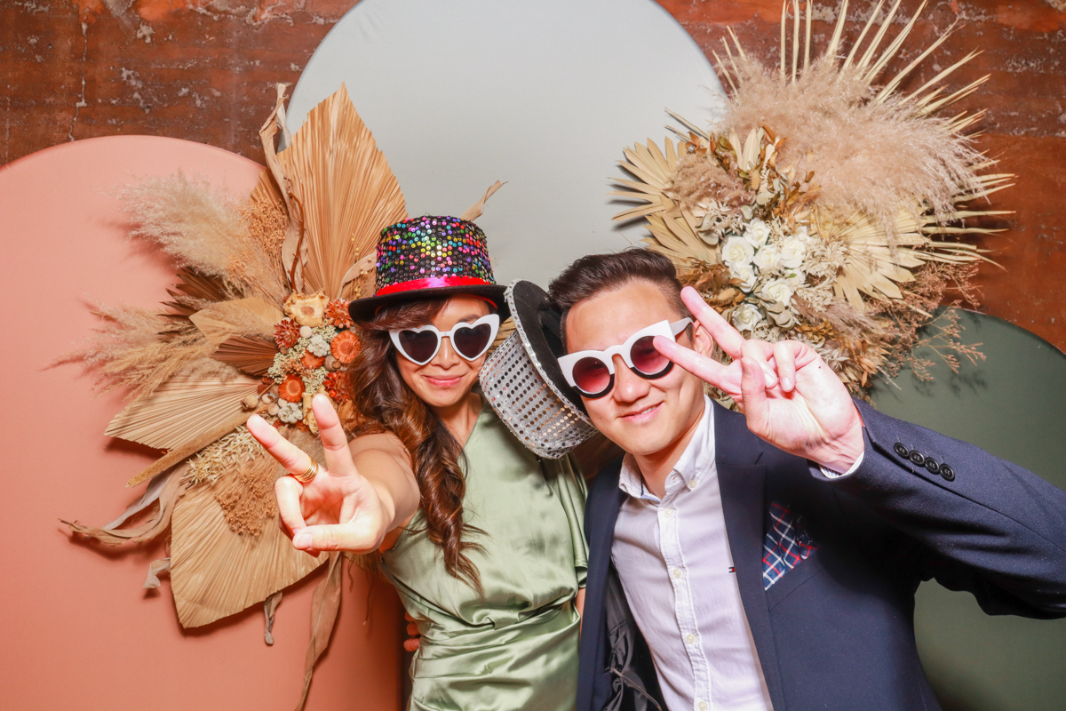 2 guests  posing against a modern arches backdrop in 3 colours, with dried flowers arrangements attached on, during an elmore court wedding venue reception party