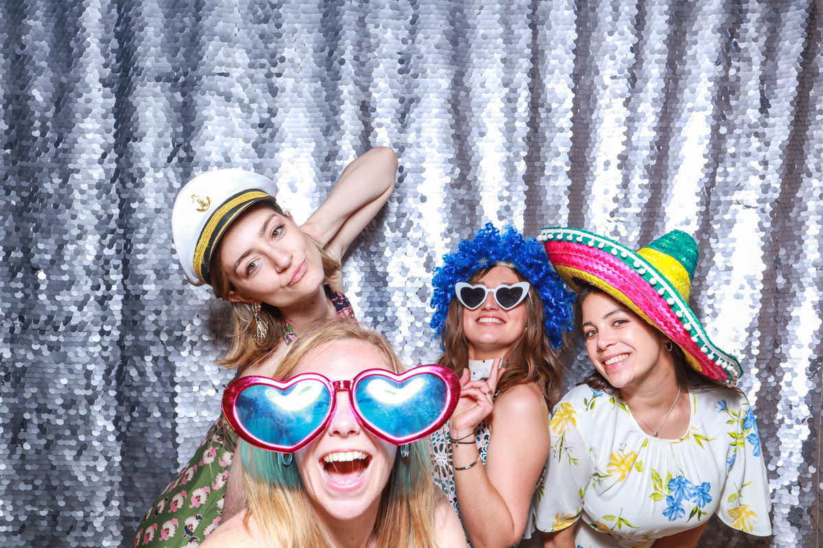 4 ladies posing with mad hat photo booth props against a sequins backdrop during a wedding reception party