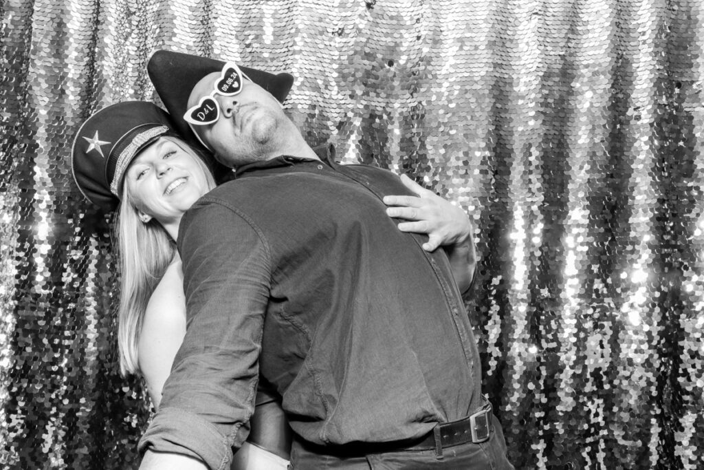 2 guests posing during the wedding party entertainment, against a silver sequins backdrop, using props and hats, at the cotswolds wedding venue