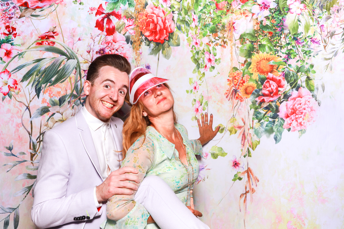 fun couple posing for a floral backdrop during the cotswolds wedding party