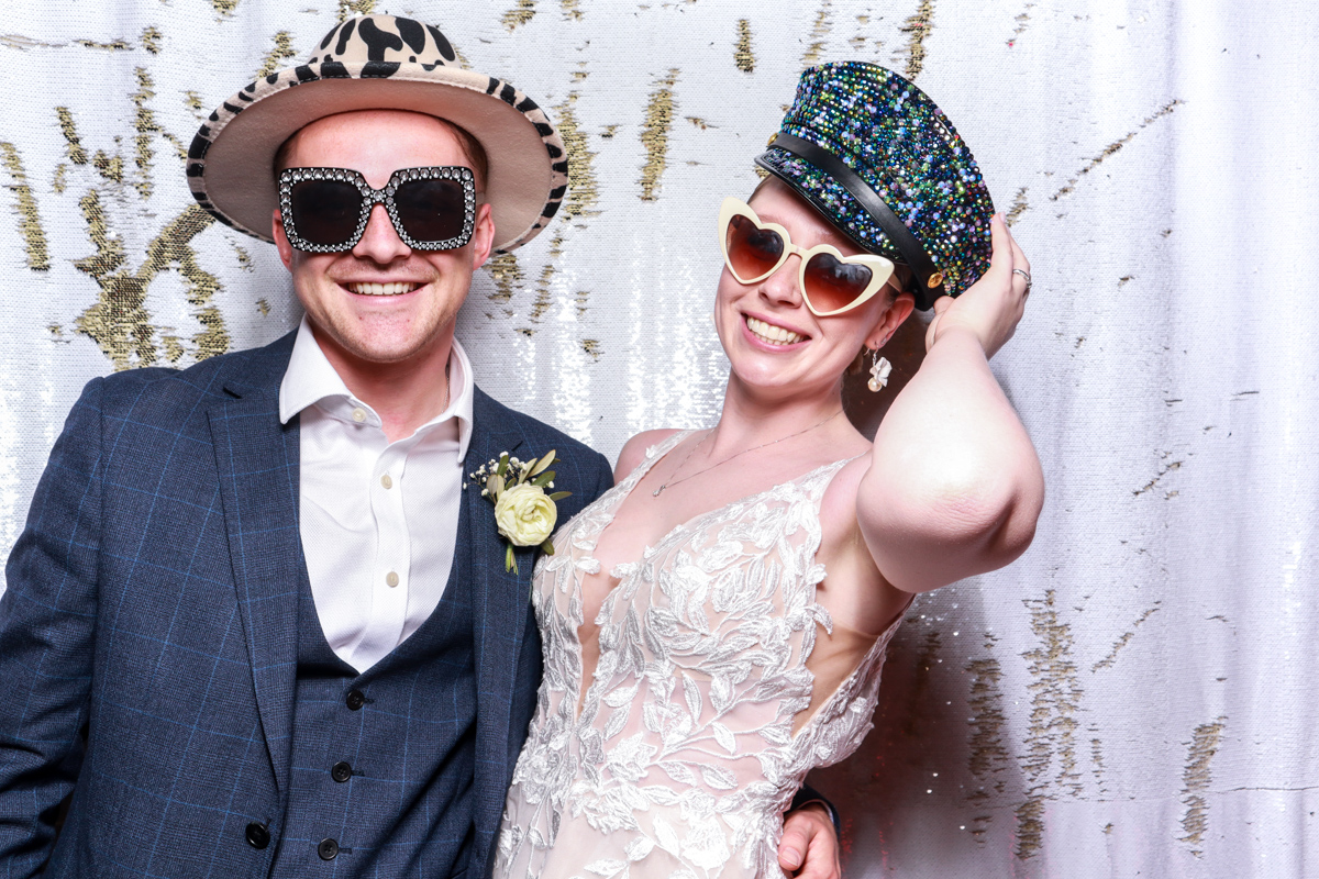 bride and groom posing during their wedding party entertainment with a reversible white and gold backdrop