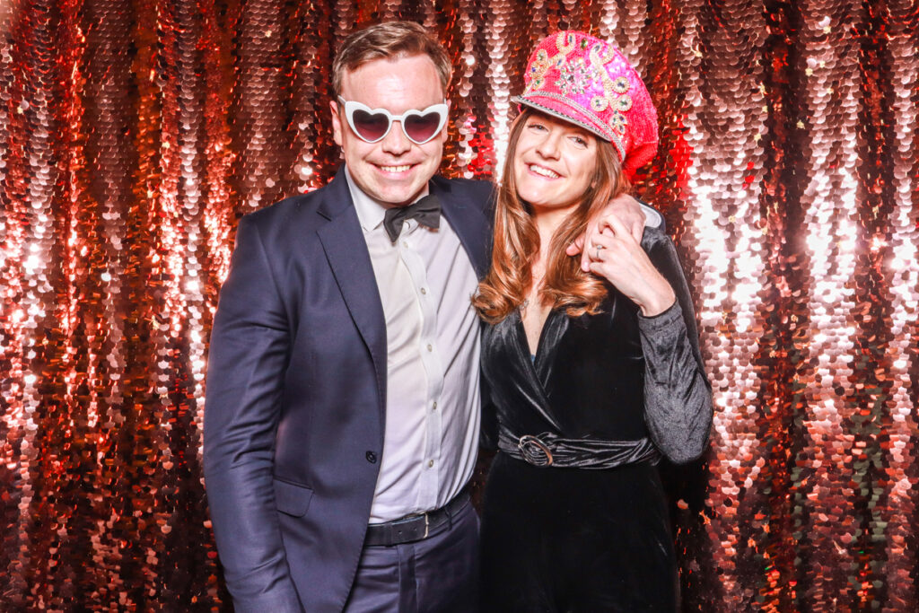 2 guests using the photo booth hire during an event, with a blush sequins backdrop and heart shaped glasses