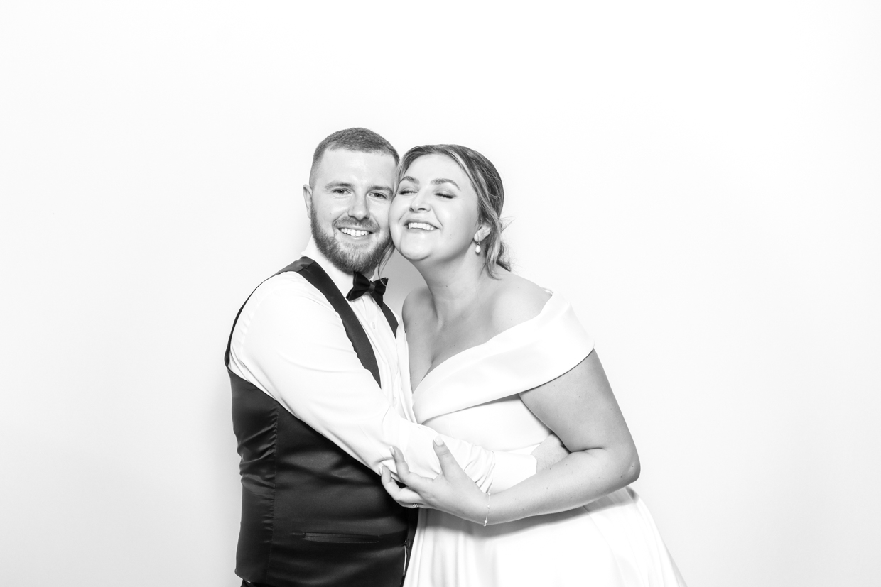 The bride and groom standing closely together, smiling with eyes closed in a loving embrace inside mad hat photo booth photo booth.