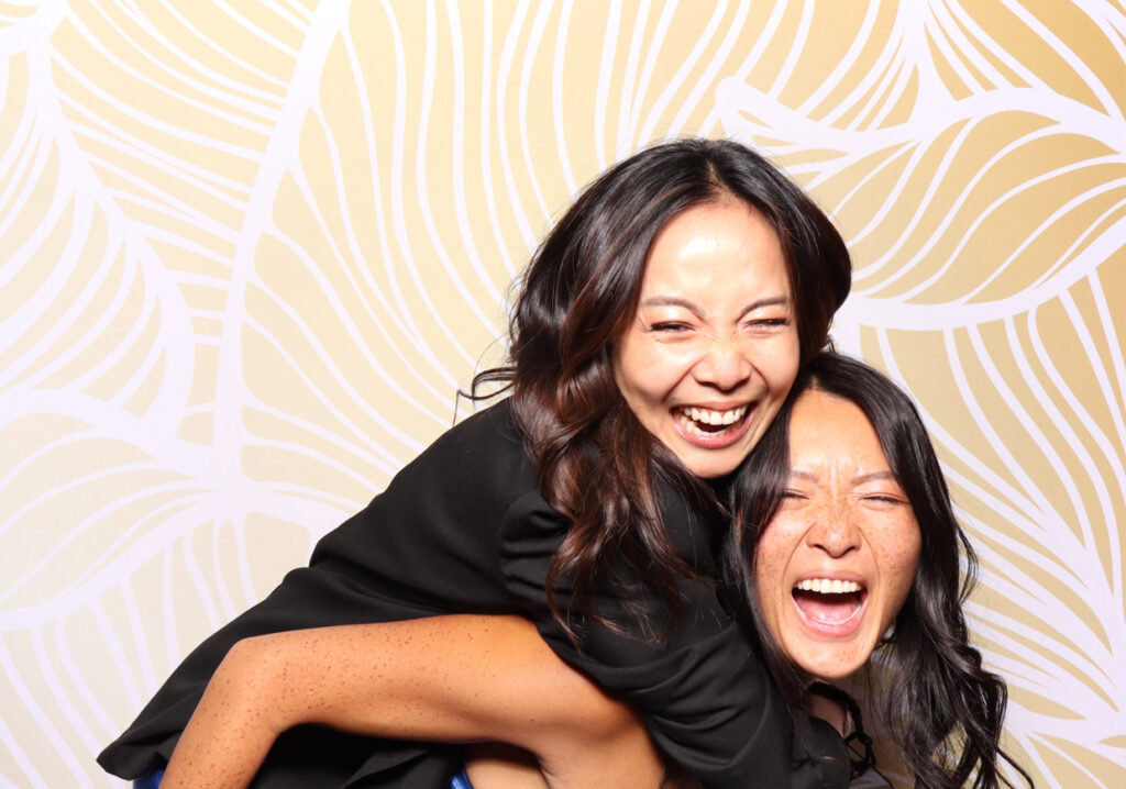 Two women laughing joyfully, with one woman giving the other a piggyback ride. Both have big smiles and are enjoying the photo booth experience at sudeley castle
