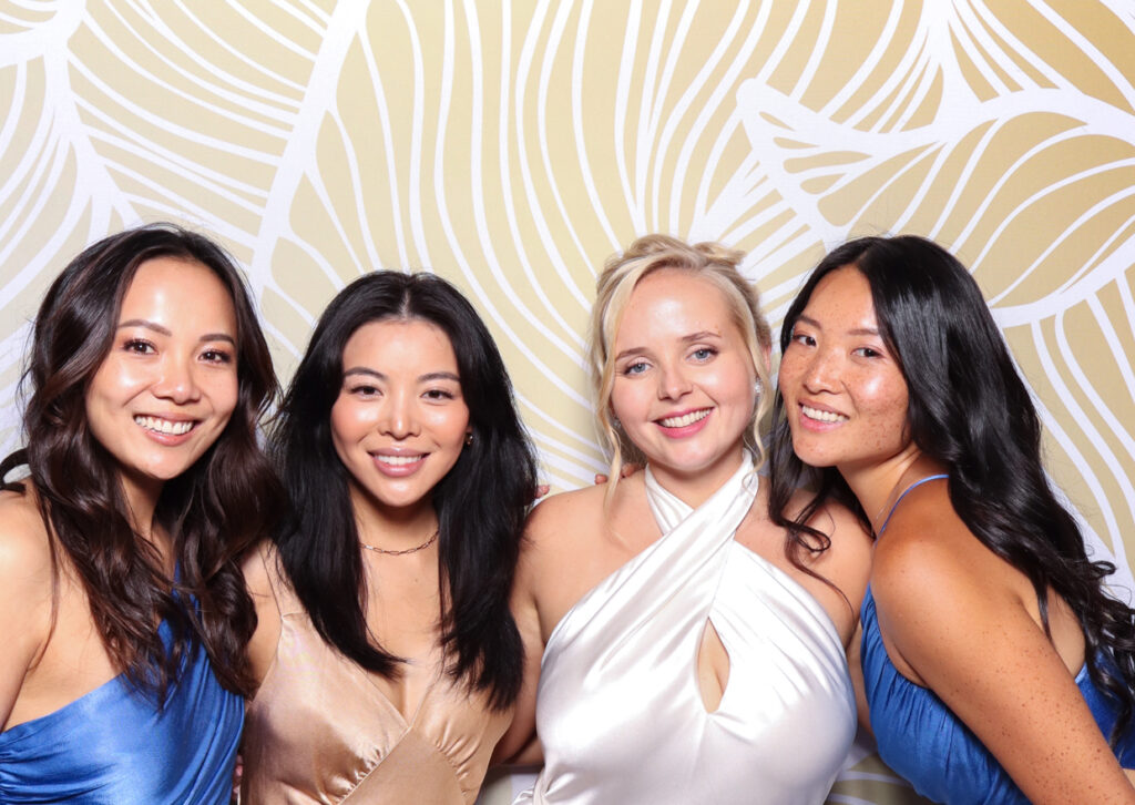 Four women, dressed in beautiful gowns, smiling and posing together. They stand close to each other, enjoying the photo booth moment  at the Sudeley Castle Wedding .