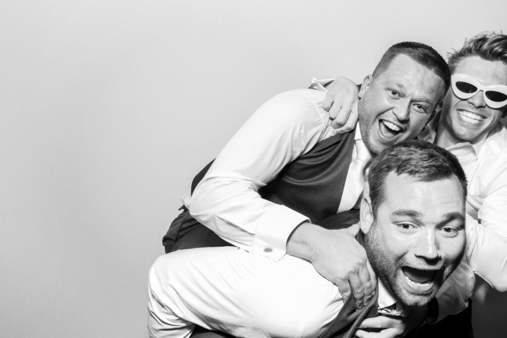 a group of 3 men jumping on top of each other during a wedding photo booth rental with the black and white filter on 