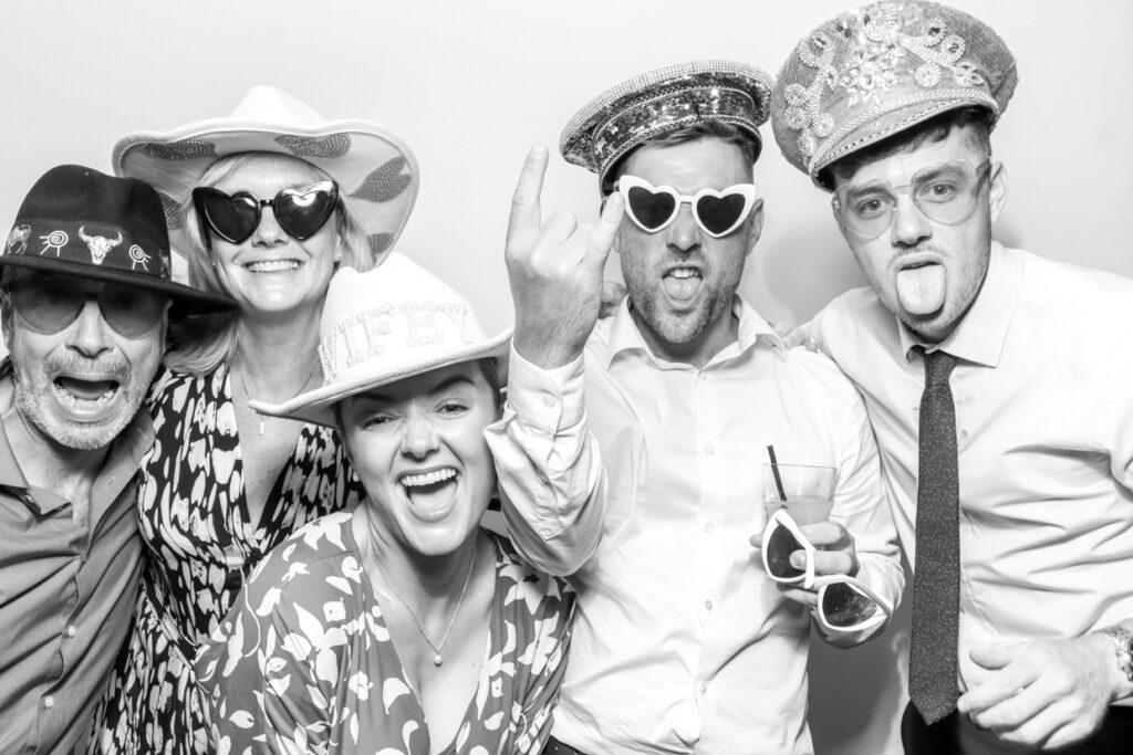 Group of wedding guests crowded into the photo booth, posing and making funny faces, capturing a joyful and lighthearted memory during a wedding photo booth party