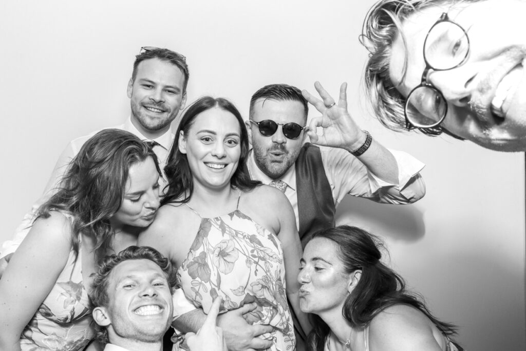 Group of wedding guests crowded into the photo booth, posing and making funny faces, capturing a joyful and lighthearted memory