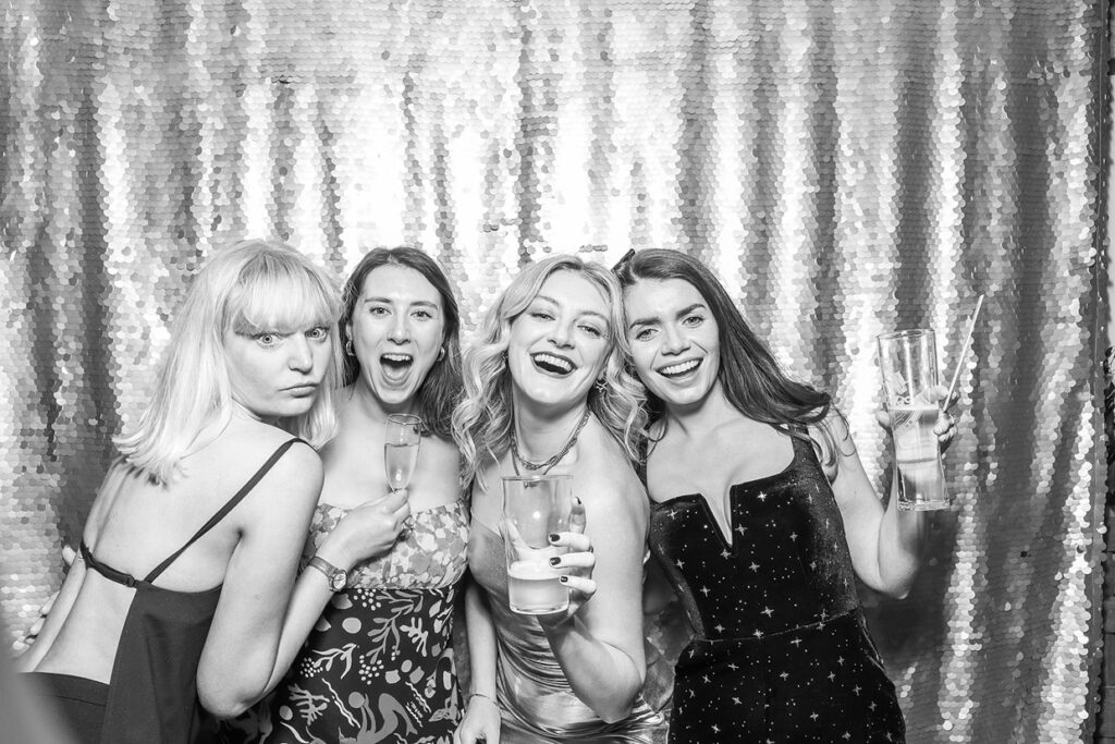 4 girls during Christmas party photo booth rental, posing against a sequins backdrop, with a b&w filter on