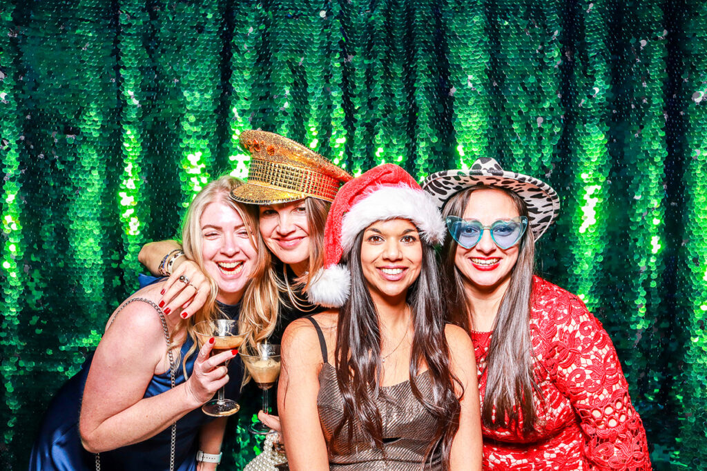 4 ladies wearing festive props, posing against a green sequins backdrop