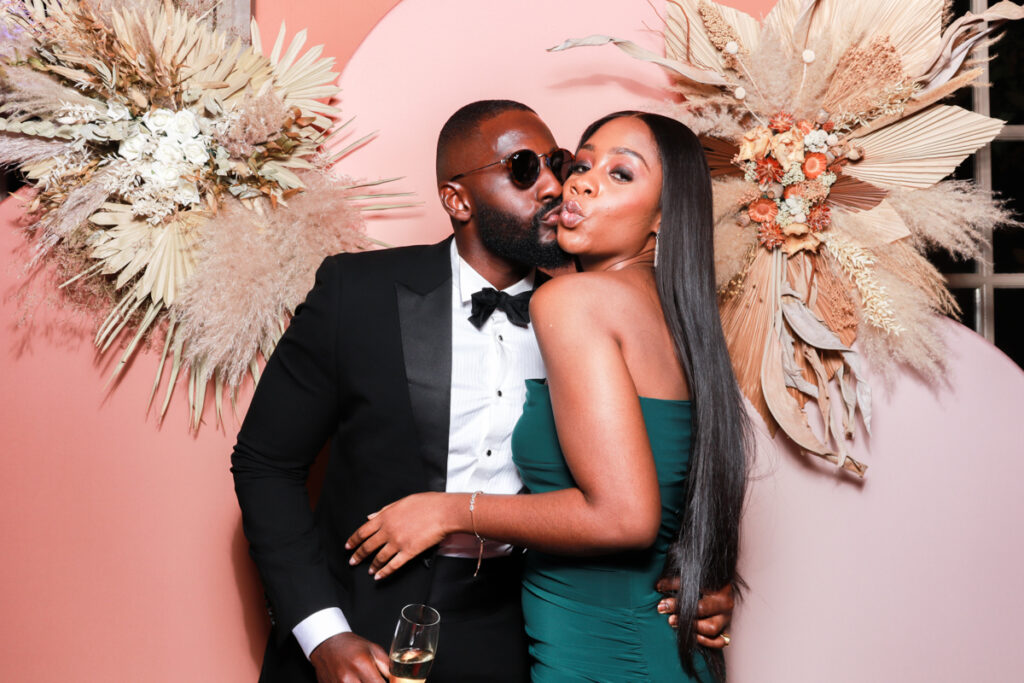 a couple kissing and posing for a photo booth rental at euridge manor, with a summer arches backdrop 