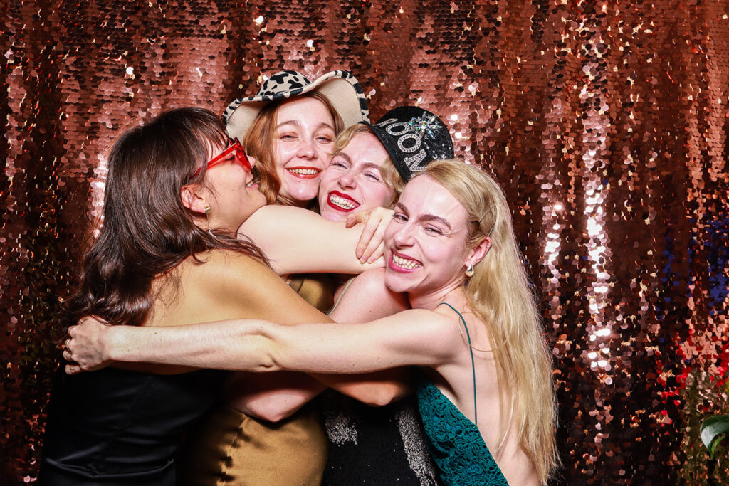 4 guests posing against a green sequins backdrop during a photo booth rental for christmas party event