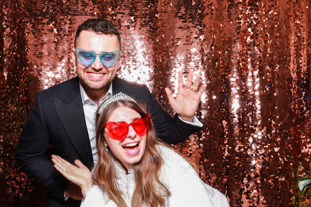 2 guests posing against a champagne sequins backdrop during a photo booth rental for christmas party event