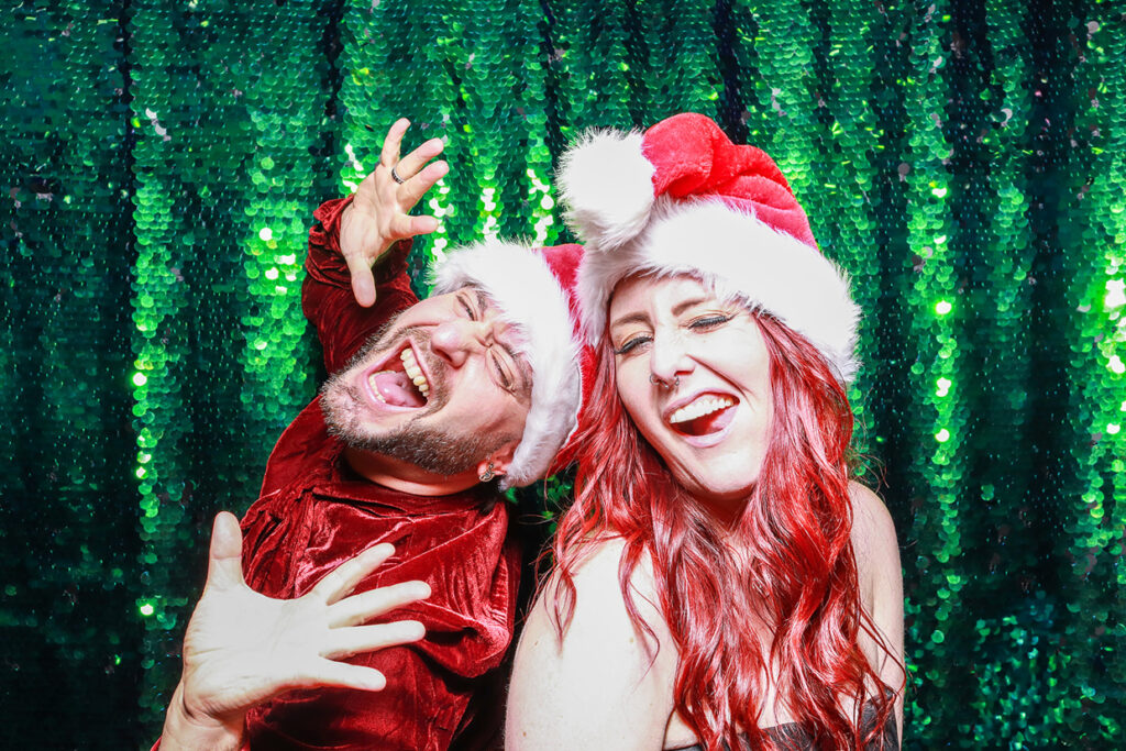 2 guests posing against a green sequins backdrop during a photo booth rental for christmas party event