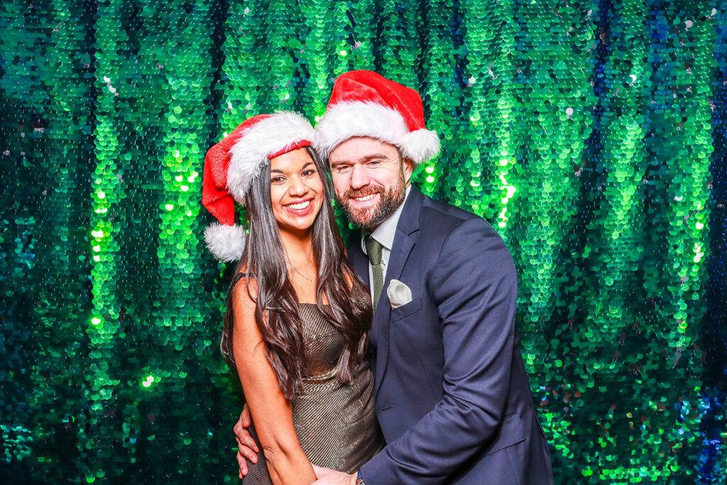 couple christmas hats posing against a green sequins backdrop during a photo booth rental with real-time social media sharing features