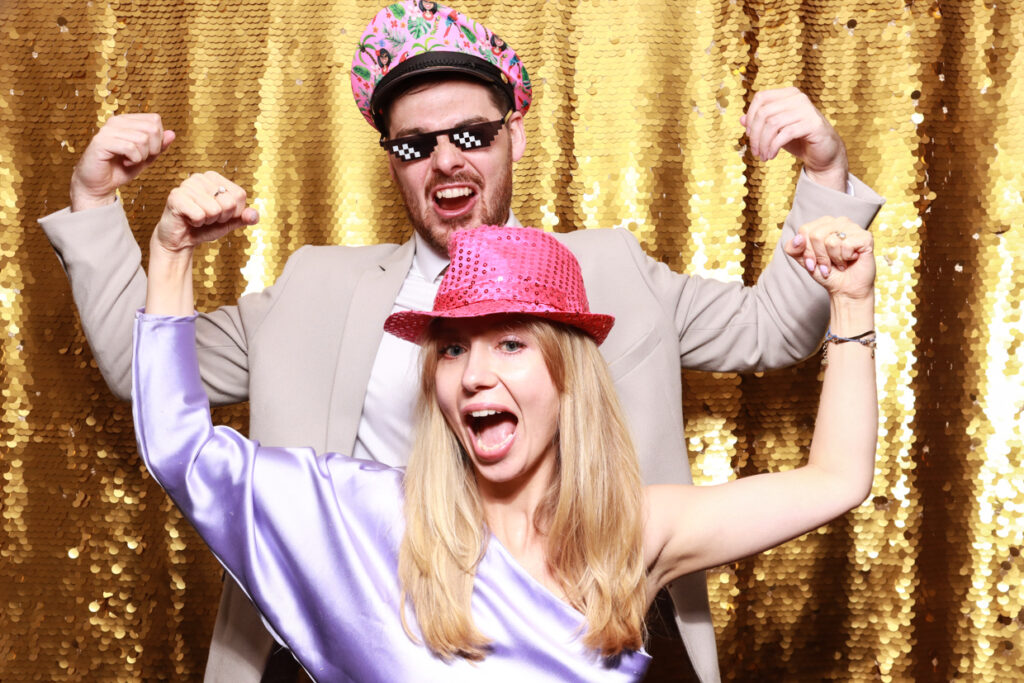 couple posing against a shiny gold backdrop during the best party entertainment in the Cotswolds