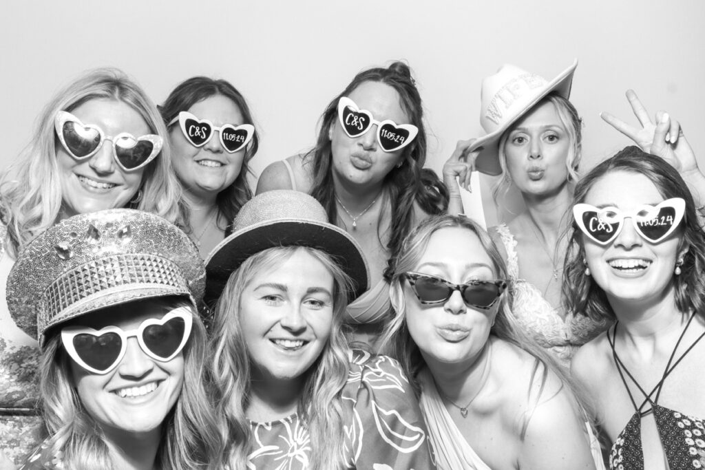 black and white pictures for a wedding event with a large group of guests wearing fun props, posing against a white backdrop