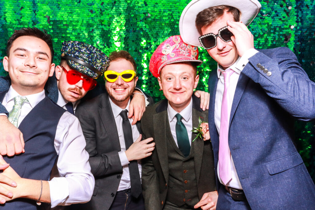 large group of guests wearing fun props and hats posing against a green sequins backdrop during a corporate party entertainment for a photo booth party rental 