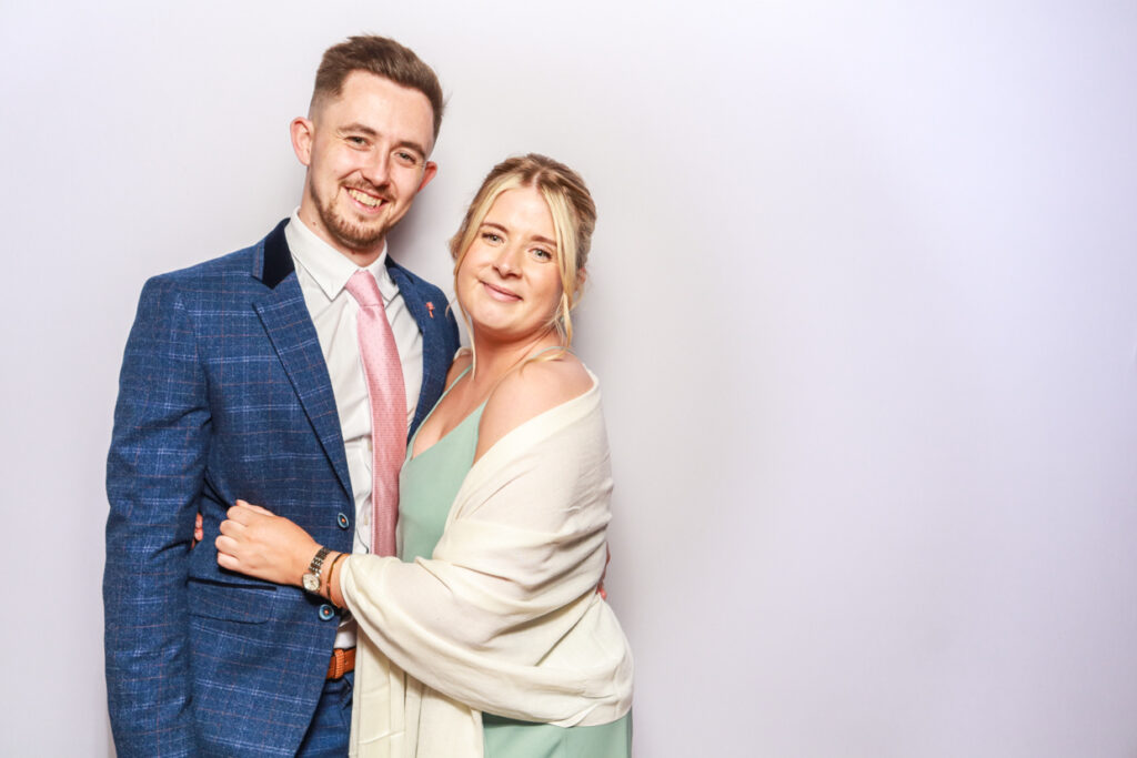 colour image of couple posing holding each other during a corporate party entertainment for a photo booth party hire with a white backdrop behind them