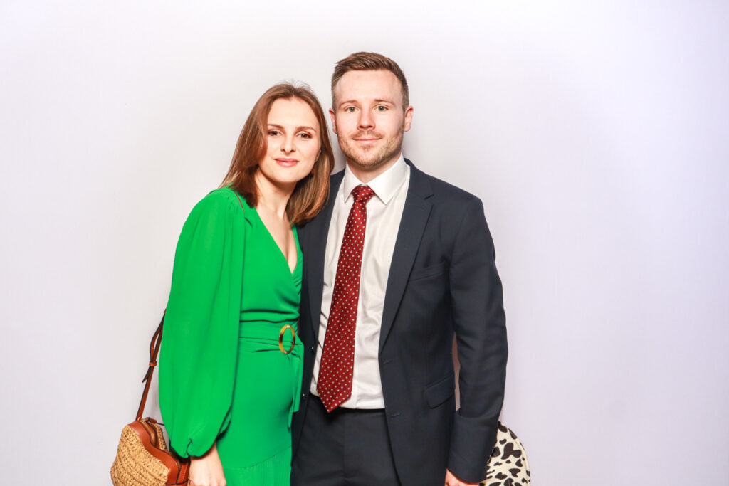 colour image of couple posing holding each other during a corporate party entertainment for a photo booth party hire with a white backdrop behind them