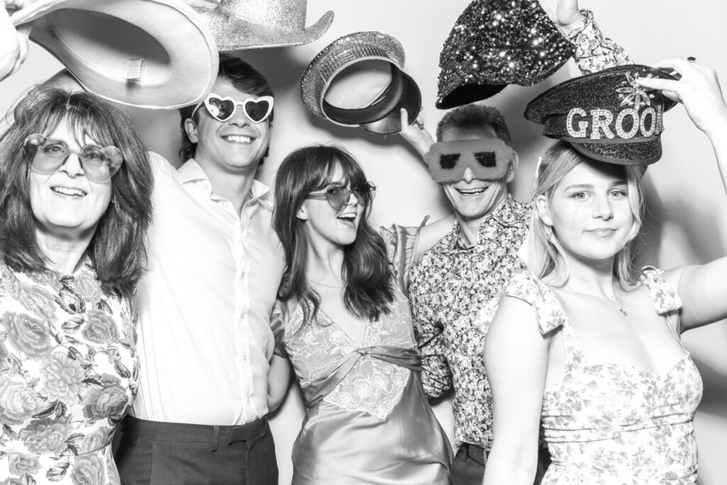 large group of people all holding their hat props up in the air, while posing for a black and white photo with a white backdrop behind them