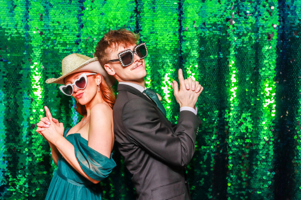 a couple posing back to back against a green sequins backdrop, during a party entertainment