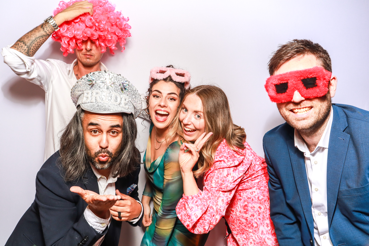 fun guests wearing props and wigs and sunglasses, posing against a white backdrop, during a reception party entertainment