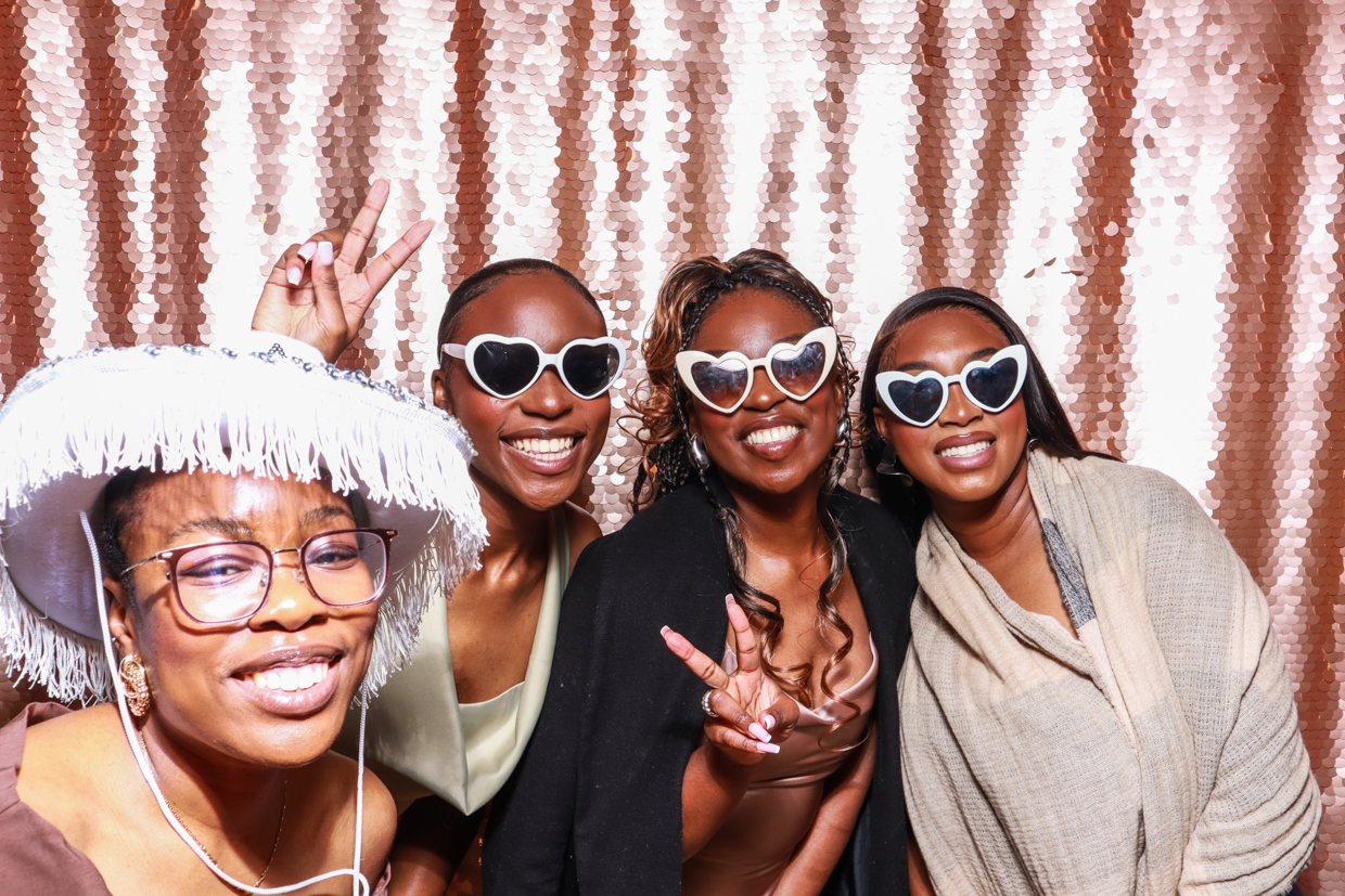 4 people posing with fun heart shaped sunglasses for the best photo booth to hire during a corporate event, against a blush sequins backdrop
