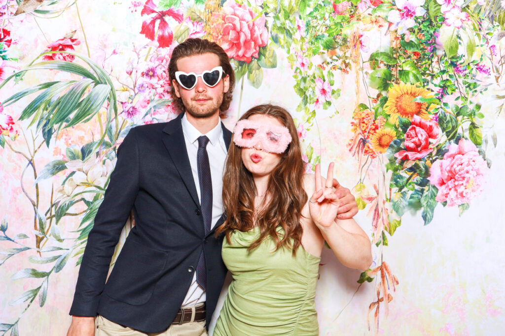 a couple posing with props against a floral backdrop, during a corporate event photo booth hire in cotswolds