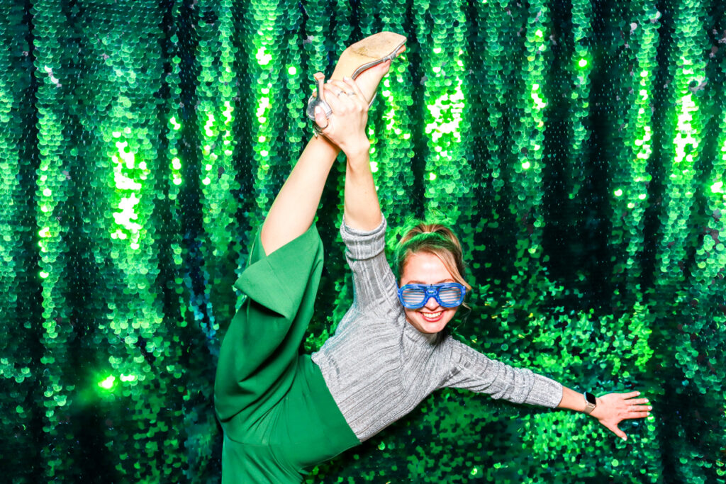 lady holding one foot up, posing against a green sequins backdrop, posing during a corporate event entertainment party , ensuring a corporate event success