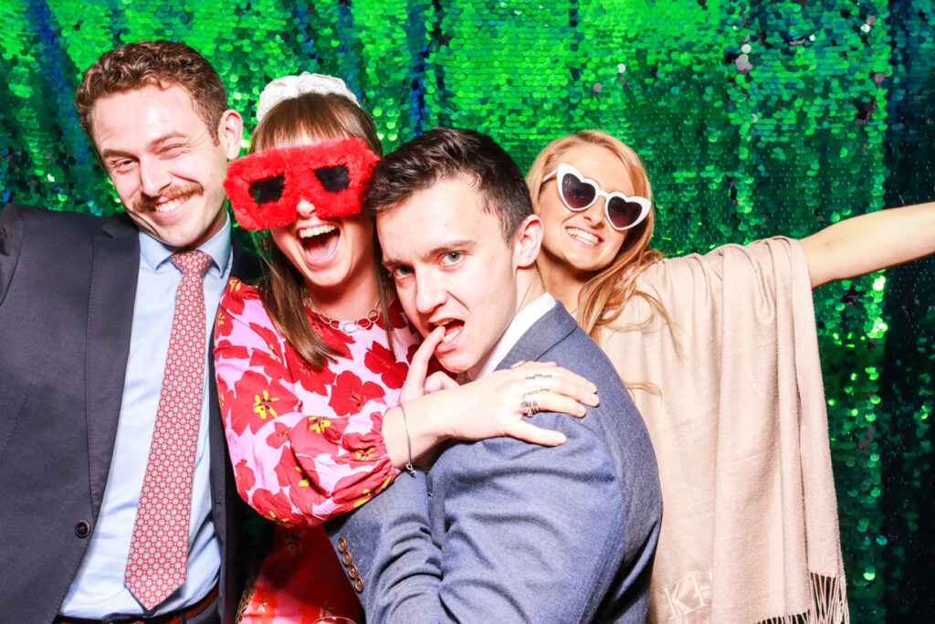 4 guests posing against a green sequins backdrop during a corporate event in the cotswolds 