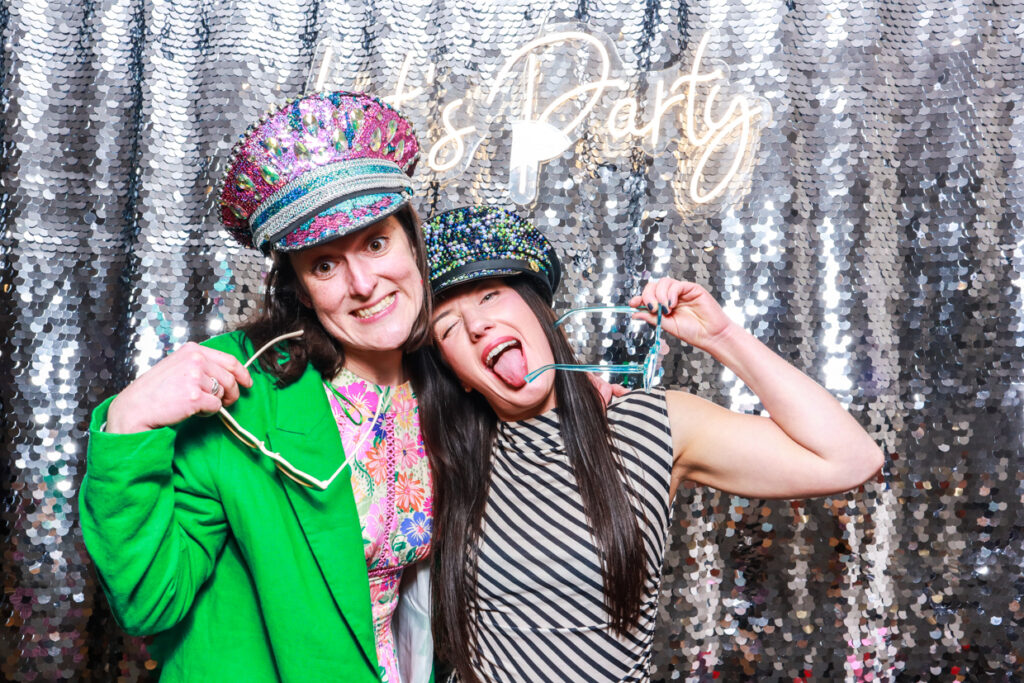 2 guests during a corporate event party entertainment, against a silver sequins backdrop and a Let's Party neon sign for a fantastic event entertainment