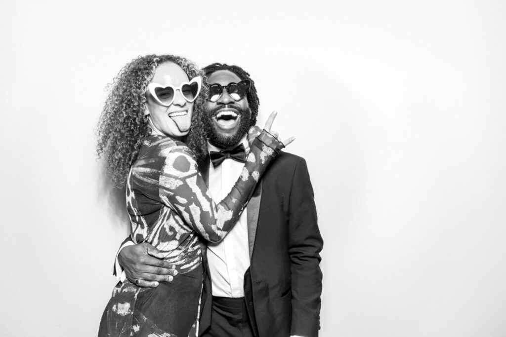 black and white photo of couple during a corporate event party entertainment, with the couple posign against a white backdrop, for a kardashian style glam unlimited print offer by mad hat photo booth